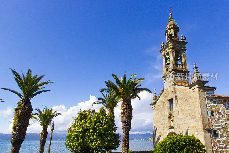 圣文森特de Noal钟楼和教堂正面在波尔图多孙，Coruña省，加利西亚，西班牙。棕榈树，海景和晴朗的天空。